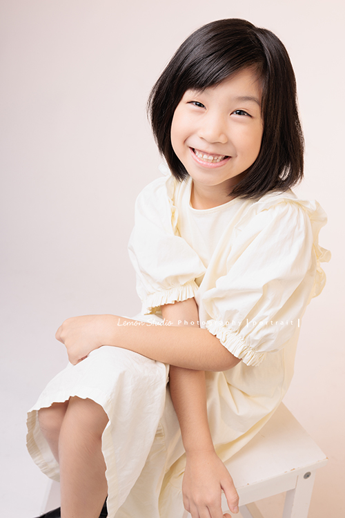 Cynthia媽麻的兩個可愛的女兒來拍寫真照，女孩們在鏡頭前很自然，拍起來不但很有質感，也抓到了兩個女孩許多不同的情緒與表情，這張是妹妹坐著看著鏡頭很有自信且笑容俏皮可愛的個人寫真！