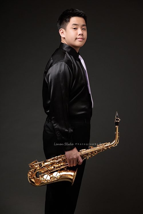 在同一個管樂團的軒＆宸兄弟檔來拍照，吹奏薩克斯風開朗的兩人，在鏡頭前很輕鬆自在地做自己，這張是哥哥軒站著單手拿著薩克斯風很帥氣地看著鏡頭的一張相片！