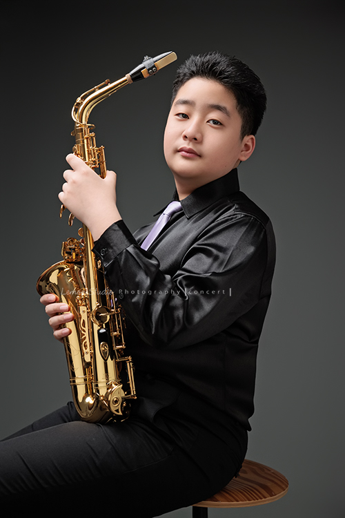 在同一個管樂團的軒＆宸兄弟檔來拍照，吹奏薩克斯風開朗的兩人，在鏡頭前很輕鬆自在地做自己，這張是弟弟宸側坐著著拿著薩克斯風看著鏡頭的一張很帥氣的相片！