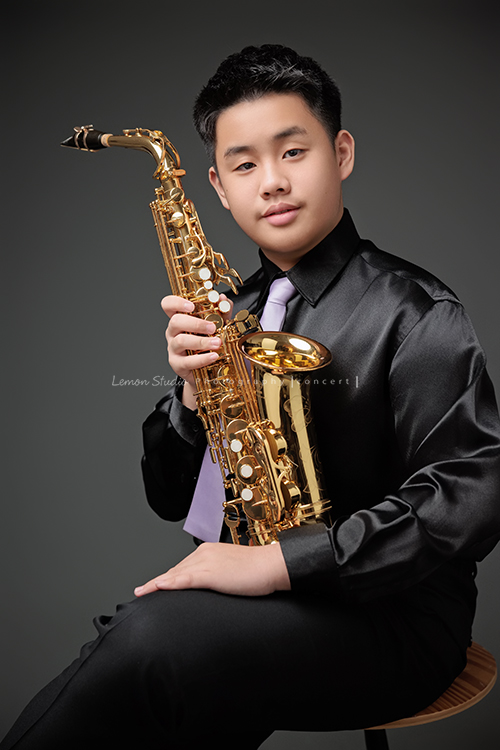 在同一個管樂團的軒＆宸兄弟檔來拍照，吹奏薩克斯風開朗的兩人，在鏡頭前很輕鬆自在地做自己，這張是哥哥軒拿著薩克斯風坐在椅子上看著鏡頭的一張很帥氣的相片！
