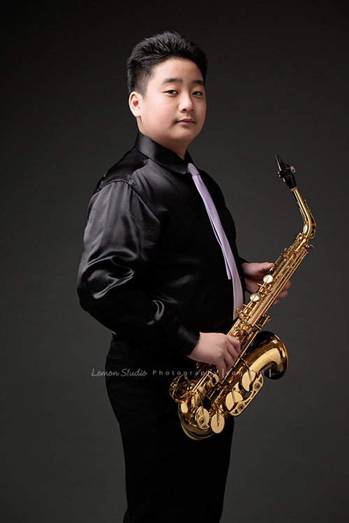 在同一個管樂團的軒＆宸兄弟檔來拍照，吹奏薩克斯風開朗的兩人，在鏡頭前很輕鬆自在地做自己，這張是弟弟宸站著拿著薩克斯風酷酷地看著鏡頭的一張很帥氣的相片