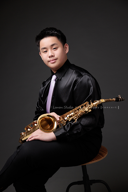 在同一個管樂團的軒＆宸兄弟檔來拍照，吹奏薩克斯風開朗的兩人，在鏡頭前很輕鬆自在地做自己，這張是哥哥軒拿著薩克斯風坐在椅子上很chill地看著鏡頭的一張很帥氣的相片！