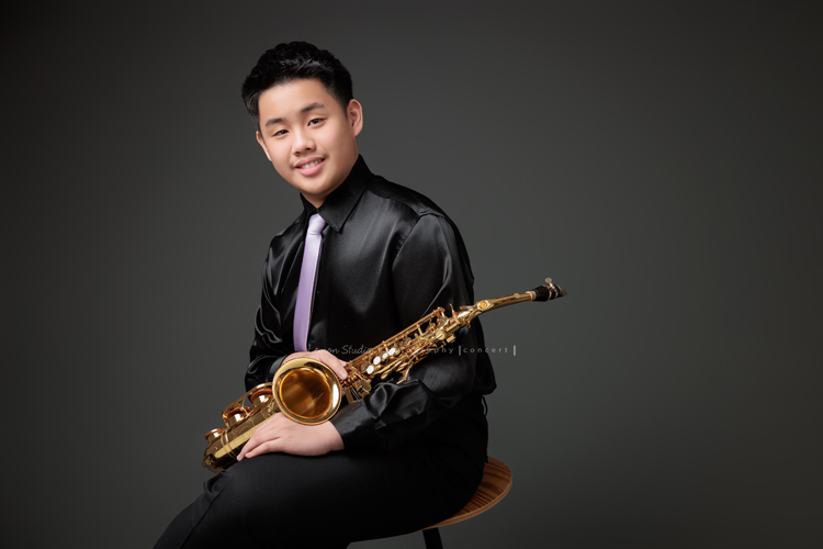 在同一個管樂團的軒＆宸兄弟檔來拍照，吹奏薩克斯風開朗的兩人，在鏡頭前很輕鬆自在地做自己，這張是哥哥軒坐著著拿著薩克斯風很有自信且沈穩地笑著的一張很帥氣的相片！
