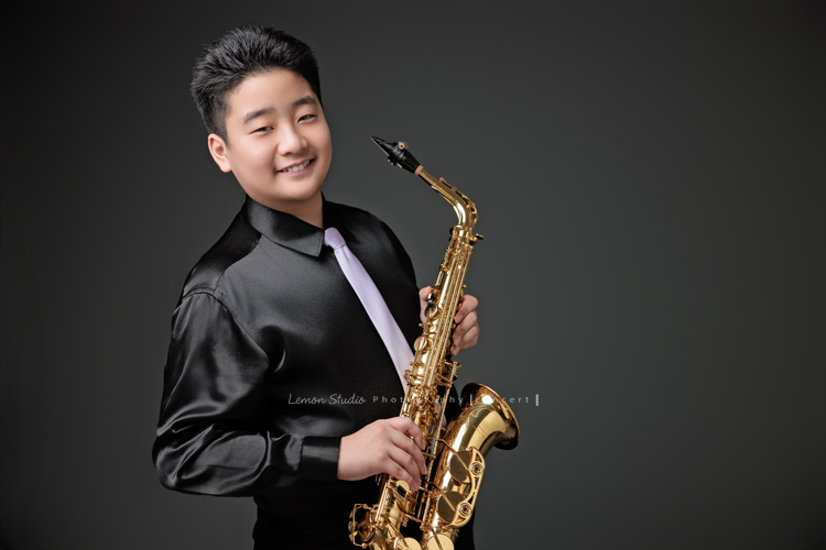 在同一個管樂團的軒＆宸兄弟檔來拍照，吹奏薩克斯風開朗的兩人，在鏡頭前很輕鬆自在地做自己，這張是弟弟宸站著拿著薩克斯風微笑地看著鏡頭的一張很帥氣的相片