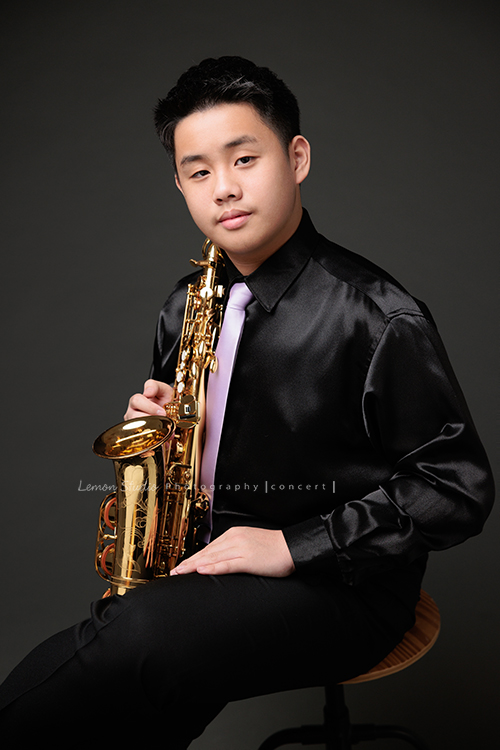 在同一個管樂團的軒＆宸兄弟檔來拍照，吹奏薩克斯風開朗的兩人，在鏡頭前很輕鬆自在地做自己，這張是哥哥軒坐著著拿著薩克斯風很有自信且沈穩地的一張很帥氣的相片！