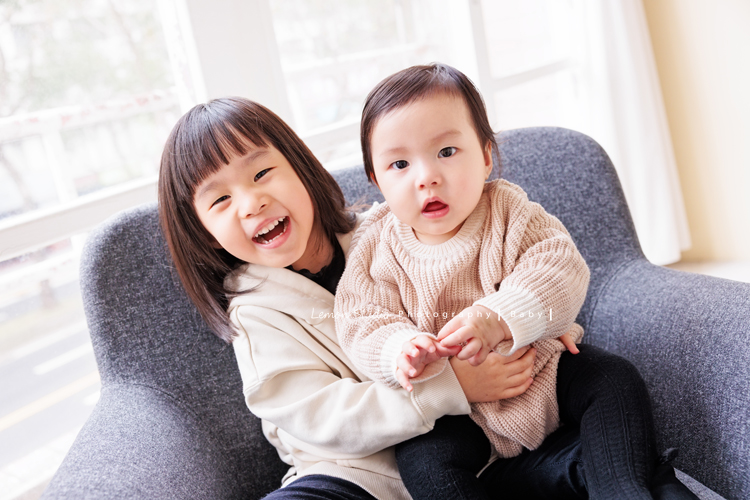 Jade媽麻一家來拍照，三歲八個月的姊姊、及八個月大的妹妹太可愛了，爸拔媽麻與姊妹倆玩得好開心，這張是姊姊抱著妹妹坐在椅子上兩人看著鏡頭的可愛姊妹倆的合照紀錄！