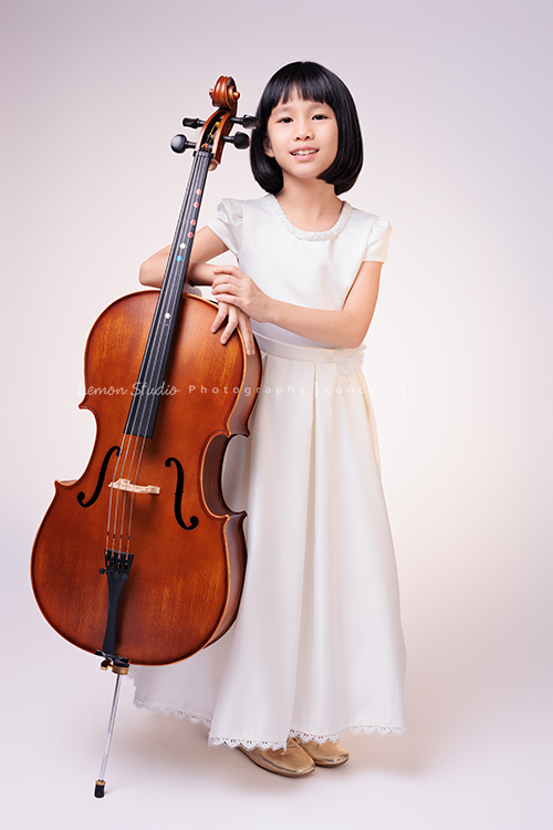 芯參加學校的弦樂團正在學習大提琴，為了即將來到的音樂會演出來拍音樂會寫真，雖然一開始拍照時有點小緊張，但逐漸地在鏡頭前越來越自在，結果捕捉到許多芯好可愛的表情及畫面，這張是芯站在大提琴旁、手扶著大提琴看著鏡頭微笑著的一張音樂會寫真照！
