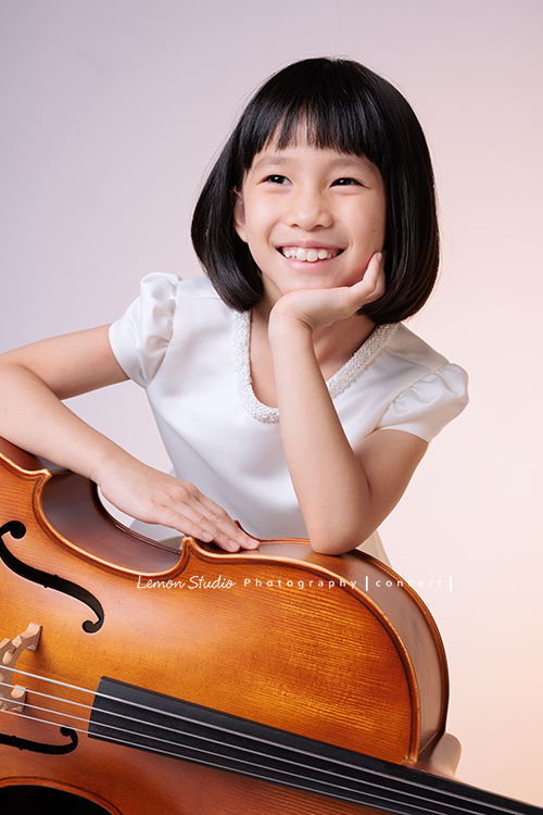 芯參加學校的弦樂團正在學習大提琴，為了即將來到的音樂會演出來拍音樂會寫真，雖然一開始拍照時有點小緊張，但逐漸地在鏡頭前越來越自在，結果捕捉到許多芯好可愛的表情及畫面，這張是芯坐著手扶在大提琴上很甜美地笑著的一張音樂會寫真照！