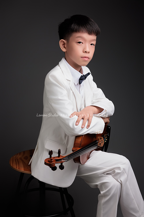 同時會拉小提琴及二胡的賢鐸來拍音樂會相片，賢鐸是學校的弦樂團A團首席及國樂全國賽特優學校二胡首席，這張是賢鐸坐在椅子上雙手放在提琴上、很有自信地看著鏡頭的音樂會相片！