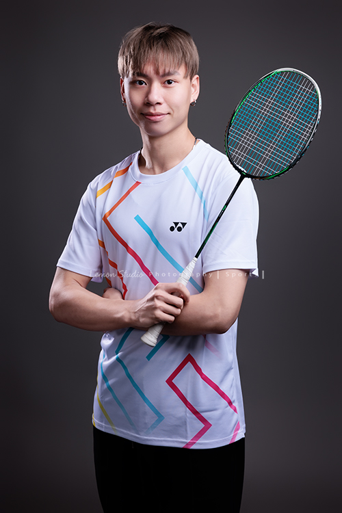 這次國小羽球隊請我們拍球隊的運動寫真照，運動的孩子們有一種很專注內斂的氣質，這次還有拍孩子們打球的瞬間，好有力量好美啊，這張是一位年輕男教練的羽球教練形象照，教練雙手抱在前面、一手拿著球拍，很沈穩地看著鏡頭！