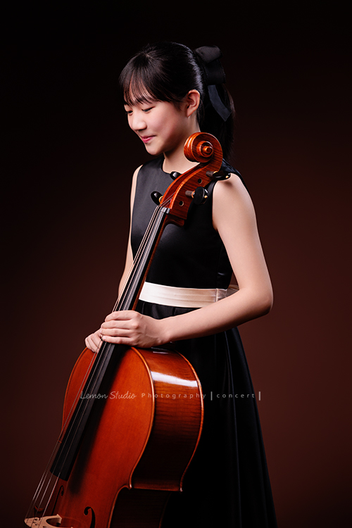 Lucie為了即將來到的音樂會帶著大提琴來拍音樂會寫真照，很有氣質的Lucie，拉琴時非常專注，Lucie笑起來很甜美，這張是Lucie站著手扶著大提琴沒有看鏡頭側身微微地低頭笑著的半身音樂會寫真照！
