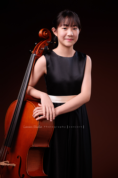 Lucie為了即將來到的音樂會帶著大提琴來拍音樂會寫真照，很有氣質的Lucie，拉琴時非常專注，Lucie笑起來很甜美，這張是Lucie站著身體靠著大提琴手輕輕扶著大提琴的七分身音樂會寫真照！Lucie很有自信地看著鏡頭，很可愛的一張音樂寫真照！