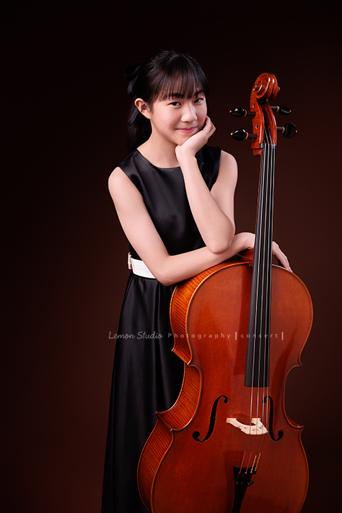Lucie為了即將來到的音樂會帶著大提琴來拍音樂會寫真照，很有氣質的Lucie，拉琴時非常專注，Lucie笑起來很甜美，這張是Lucie站著手扶著大提琴的七分身音樂會寫真照！Lucie一手扶大提琴、另一手托住下巴，很俏皮地看著鏡頭！