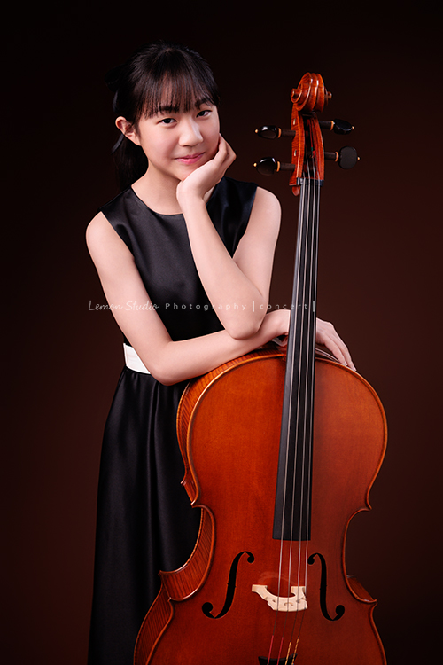 Lucie為了即將來到的音樂會帶著大提琴來拍音樂會寫真照，很有氣質的Lucie，拉琴時非常專注，Lucie笑起來很甜美，這張是Lucie站著手扶著大提琴的七分身音樂會寫真照！Lucie一手扶大提琴、另一手托住下巴，微微地笑著看著鏡頭！