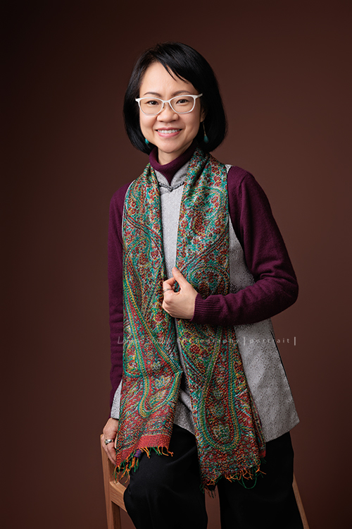 大學教授Joy來拍形象照，Joy教授帶了很美很藝術氣息的服飾來拍照，這張是Joy在搭配的衣服上加一個很民族風的圍巾，配上白色鏡框，一手放在圍巾上、一手放在椅子上，對著鏡頭微笑的一張很美的教授個人形象照！