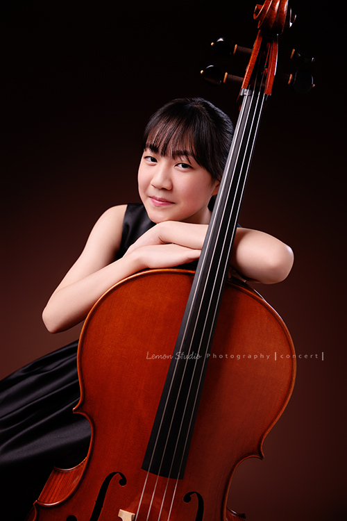 Lucie為了即將來到的音樂會帶著大提琴來拍音樂會寫真照，很有氣質的Lucie，笑起來很甜美，這張是Lucie坐在椅子上，雙手輕輕扶著大提琴，臉靠在手上，臉稍微側一邊對著鏡頭甜美地微笑的模樣！