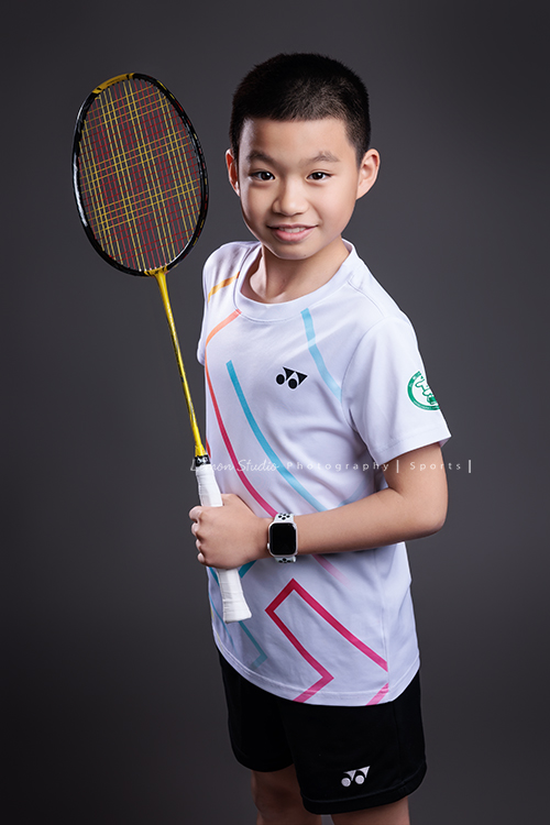 這次國小羽球隊請我們拍球隊的運動寫真照，運動的孩子們有一種很專注內斂的氣質，這次還有拍孩子們打球的瞬間，好有力量好美啊，這張是羽球隊裡一位男孩的運動寫真照，男孩一手拿球拍、一手叉腰，看著鏡頭微笑、很帥氣！