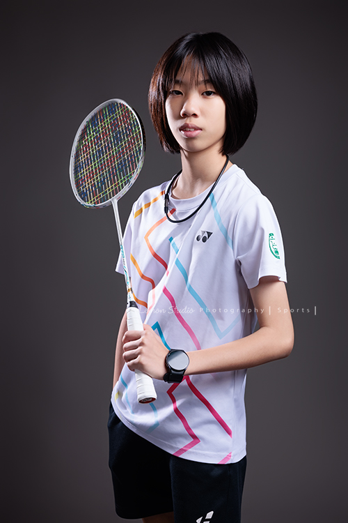 這次國小羽球隊請我們拍球隊的運動寫真照，運動的孩子們有一種很專注內斂的氣質，這次還有拍孩子們打球的瞬間，好有力量好美啊，這張是羽球隊裡一位女孩的運動寫真照，女孩一手拿球拍、一手放口袋，酷酷地看著鏡頭、很帥氣！