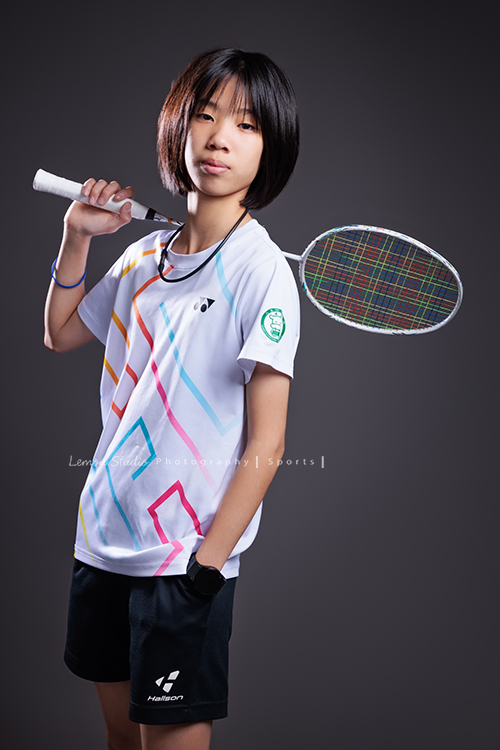 這次國小羽球隊請我們拍球隊的運動寫真照，運動的孩子們有一種很專注內斂的氣質，這次還有拍孩子們打球的瞬間，好有力量好美啊，這張是羽球隊裡一位女孩的運動寫真照，女孩一手拿球拍放在肩膀上、一手放口袋，酷酷地看著鏡頭、很帥氣！