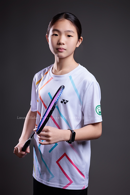 這次國小羽球隊請我們拍球隊的運動寫真照，運動的孩子們有一種很專注內斂的氣質，這次還有拍孩子們打球的瞬間，好有力量好美啊，這張是羽球隊裡一位女孩的運動寫真照，女孩兩手拿球拍、很酷地看著鏡頭！