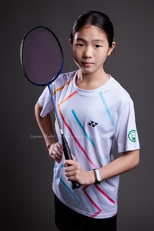 這次國小羽球隊請我們拍球隊的運動寫真照，運動的孩子們有一種很專注內斂的氣質，這次還有拍孩子們打球的瞬間，好有力量好美啊，這張是羽球隊裡一位女孩的運動寫真照，女孩一手拿球拍、一手叉腰、很酷地看著鏡頭！