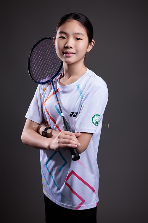 這次國小羽球隊請我們拍球隊的運動寫真照，運動的孩子們有一種很專注內斂的氣質，這次還有拍孩子們打球的瞬間，好有力量好美啊，這張是羽球隊裡一位女孩的運動寫真照，女孩一手拿球拍、兩手抱著胸前、微微地笑著看著鏡頭！