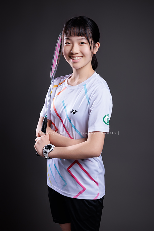 這次國小羽球隊請我們拍球隊的運動寫真照，運動的孩子們有一種很專注內斂的氣質，這次還有拍孩子們打球的瞬間，好有力量好美啊，這張是羽球隊裡一位女孩的運動寫真照，女孩一手拿著球拍、雙手環繞在前面，笑得很甜美地看著鏡頭！