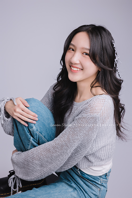 姊姊和妹妹分別來拍個人寫真，笑起來很甜美的姊姊很自在地做自己，在鏡頭前留下屬於這一刻的青春，這張是姊姊坐在椅子上、抬起一腳、兩手抱著腳、看著鏡頭笑得很甜美的個人寫真！