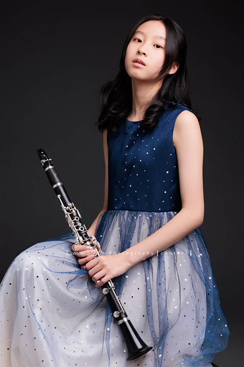 為了即將登場的音樂會，瑄帶著她的豎笛來拍攝音樂會寫真，穿上優雅的藍色系禮服，舉手投足間流露出屬於她的從容與氣質，這張是瑄坐著雙手扶拿著豎笛下巴些微抬高，帶著空靈的氣質看著鏡頭的美麗模樣！