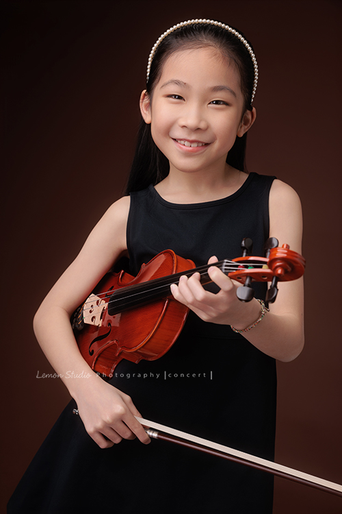 剛考上音樂班的軒，帶著她心愛的小提琴來拍音樂寫真照，一身黑色小洋裝，氣質滿滿又甜美可愛，站在鏡頭前的她個子小小的，卻閃耀著屬於自己的光芒，這一天為她的努力留下美好的紀念，這張是軒手拿著提琴和琴弓，看著鏡頭很甜美地笑著的音樂寫真照！