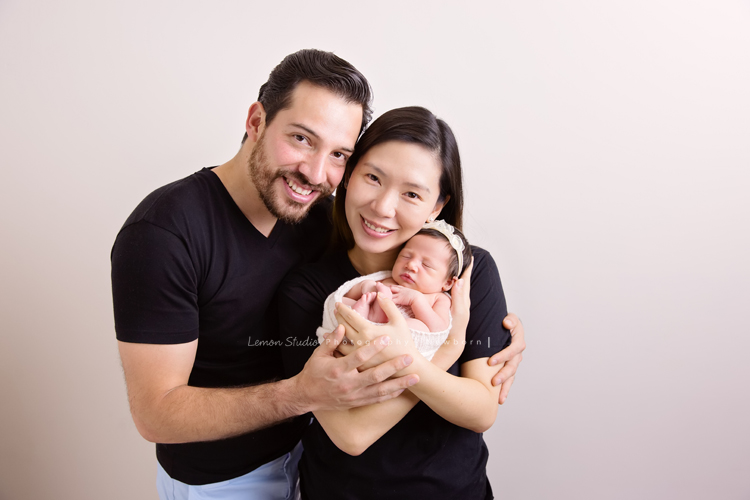 Diana媽麻和先生帶著剛出生的寶寶來拍新生兒攝影，外國人的爸拔和媽麻一起抱著寶寶，三人之間的互動自然又真摯，這是他們第一次的全家福，也是送給寶寶最有溫度美好的出生禮物，這張是爸拔媽麻將寶寶抱在他們兩人的前方，兩人充滿愛地抱著寶寶看著鏡頭微笑的幸福模樣！