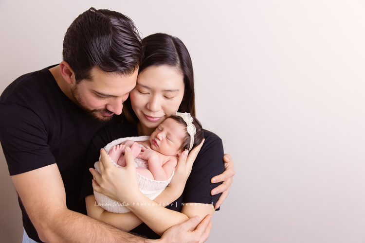 Diana媽麻和先生帶著剛出生的寶寶來拍新生兒攝影，外國人的爸拔和媽麻一起抱著寶寶，三人之間的互動自然又真摯，這是他們第一次的全家福，也是送給寶寶最有溫度美好的出生禮物，這張是爸拔媽麻將寶寶抱在他們兩人的前方，爸拔媽麻閉著雙眼兩人充滿愛地抱著寶寶的幸福模樣！