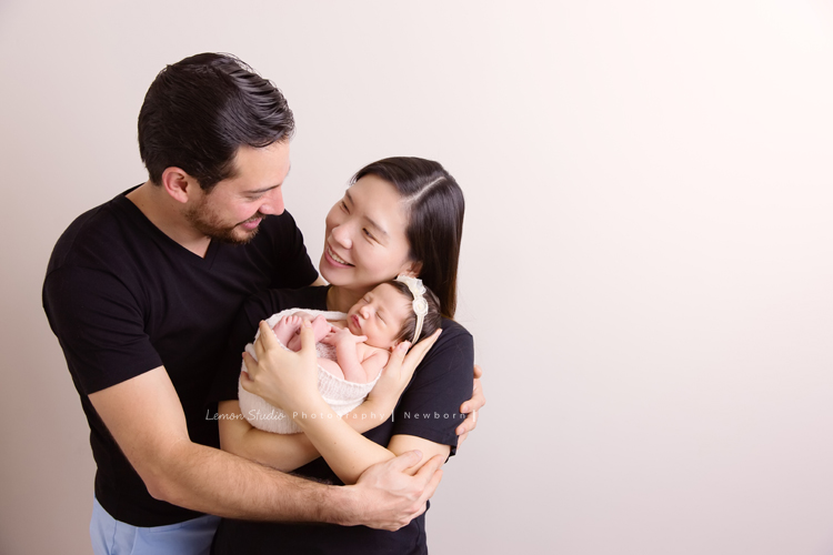 Diana媽麻和先生帶著剛出生的寶寶來拍新生兒攝影，外國人的爸拔和媽麻一起抱著寶寶，三人之間的互動自然又真摯，這是他們第一次的全家福，也是送給寶寶最有溫度美好的出生禮物，這張是爸拔媽麻將寶寶抱在他們兩人的前方，兩人充滿愛地抱著寶寶、爸拔媽麻看著彼此微笑的幸福模樣！