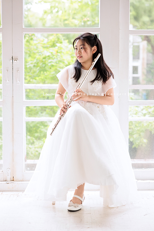 宥欣自小喜愛長笛，樂於在台上演出並與大家分享美好的音樂，9歲時即以非凡的音樂表現脫穎而出，成為台灣歷年來長笛組最年輕首位榮獲日本第33回古典音樂大賽全國大會總決賽長笛部國小中年級最高名次，今年剛滿11歲的她，將於11月底舉辦人生中的第一場獨奏會，有興趣的人可以留言跟我們索票喔，這張是宥欣穿著白色禮服坐在椅子上雙手拿著長笛，沒有看著鏡頭，很有意境的一張長笛音樂寫真！