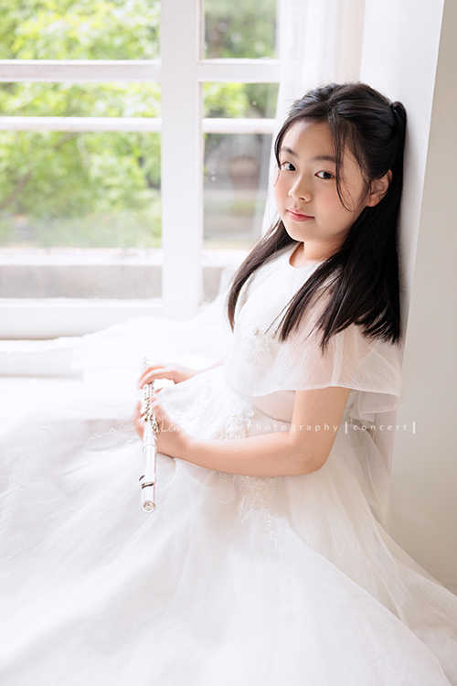 宥欣自小喜愛長笛，樂於在台上演出並與大家分享美好的音樂，9歲時即以非凡的音樂表現脫穎而出，成為台灣歷年來長笛組最年輕首位榮獲日本第33回古典音樂大賽全國大會總決賽長笛部國小中年級最高名次，今年剛滿11歲的她，將於11月底舉辦人生中的第一場獨奏會，有興趣的人可以留言跟我們索票喔，這張是宥欣穿著白色禮服雙手拿著長笛，坐在地上靠著牆，看著鏡頭的一張長笛音樂寫真！