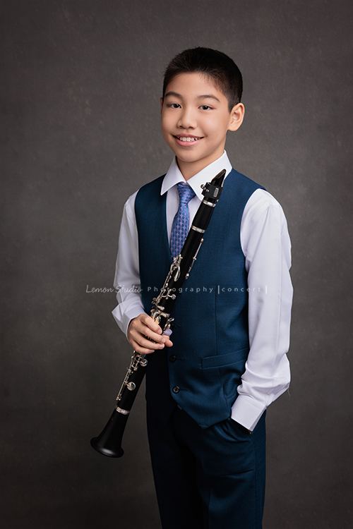 圻和同學們即將舉辦一場音樂會，身為管樂團的一員圻吹奏的是豎笛，換上西裝的圻多了份帥氣與沉穩，鏡頭裡的他自信而有氣質，這張是圻一手拿著豎笛、一手放在口袋裡、對著鏡頭微笑的音樂會相片！
