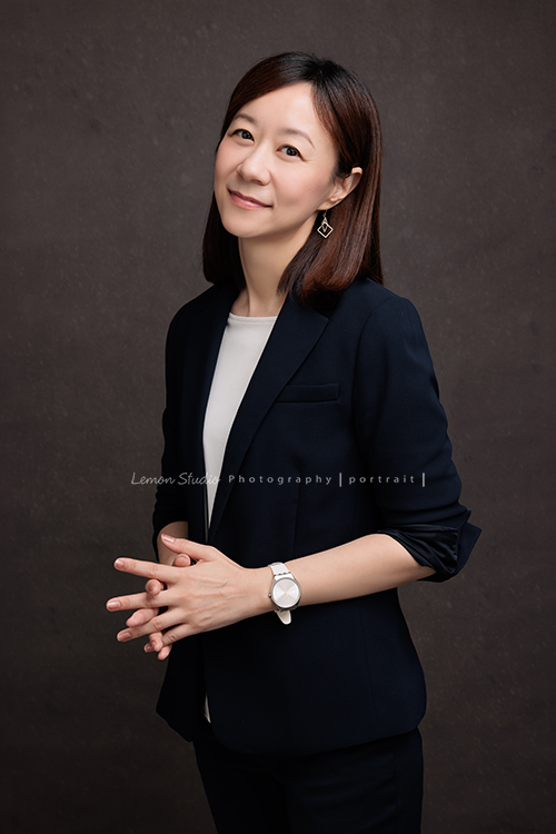 來自零售產業的品芳來拍形象照，品芳親切又隨和，在鏡頭前展現出屬於自己的自信與魅力，照片中流露出她沈穩及自在的氣質，這張是品芳雙手在身體前方自然地交叉，沈穩地看著鏡頭微笑！很優雅的一張相片！