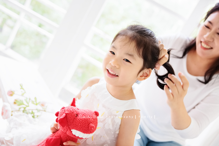 Jess媽一家第三次來拍照，這次是為了紀念雅滿四歲的時光，一家人總是自然又自在，照片裡流露出的，是日常中最真實舒服的模樣，這張是雅穿白色洋裝、媽麻在她身後綁她的頭髮的小紀錄！當下兩人都笑得很開心啊！