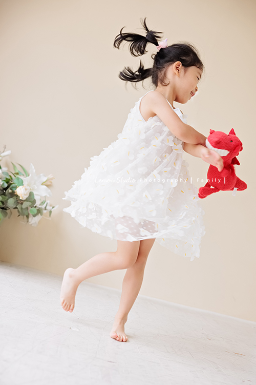 Jess媽一家第三次來拍照，這次是為了紀念雅滿四歲的時光，一家人總是自然又自在，照片裡流露出的，是日常中最真實舒服的模樣，這張是雅穿白色洋裝、手抱著紅色的娃娃正在跳舞的雅！