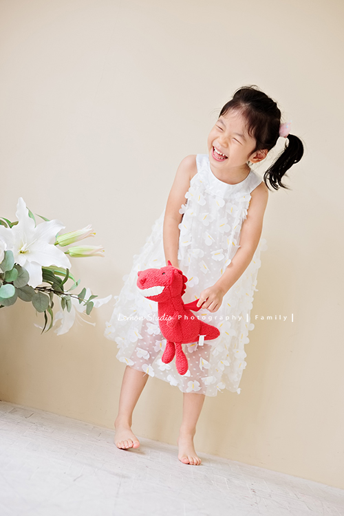 Jess媽一家第三次來拍照，這次是為了紀念雅滿四歲的時光，一家人總是自然又自在，照片裡流露出的，是日常中最真實舒服的模樣，這張是雅穿白色洋裝、手拿著一隻紅色的娃娃，看著窗外笑得超級開心的模樣！