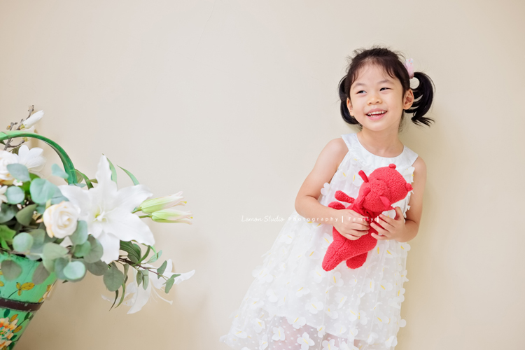 Jess媽一家第三次來拍照，這次是為了紀念雅滿四歲的時光，一家人總是自然又自在，照片裡流露出的，是日常中最真實舒服的模樣，這張是雅穿白色洋裝、手抱著紅色的娃娃，看著窗外笑得很甜美的模樣！