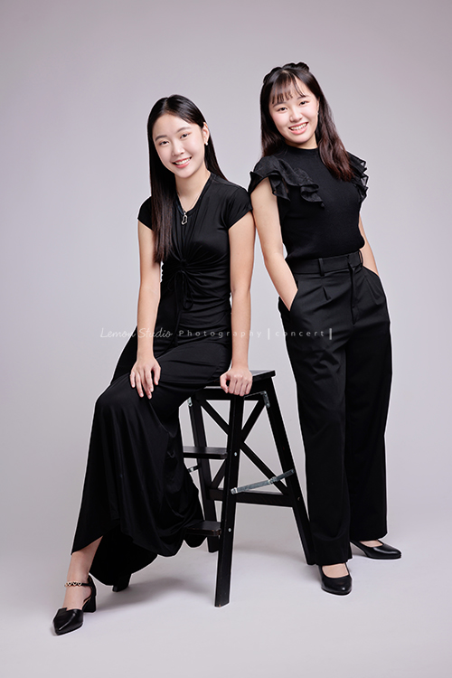 就讀高中音樂班的樂&妤，為了要辦的提琴音樂會，特地來拍攝音樂會寫真，兩人不僅默契十足，更散發著溫柔而有氣質的光彩，這張是樂坐在椅子上、妤站著、兩人都穿黑色系的衣服、兩人對著鏡頭微笑的音樂會寫真合照！