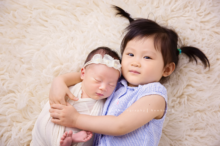琄媽麻第二個寶貝的新生兒寫真，兩歲的小姊姊展現出滿滿的愛與呵護，小小的手輕輕撫摸著妹妹好有愛，而寶寶那努力撐著小頭的模樣，真是讓人一看就融化，怎麼看都看不膩，這張是寶寶包在白色的布裡、頭上戴著有白色的花的髮帶，小姊姊躺在寶寶旁邊溫柔地抱著寶寶的兩人合照！