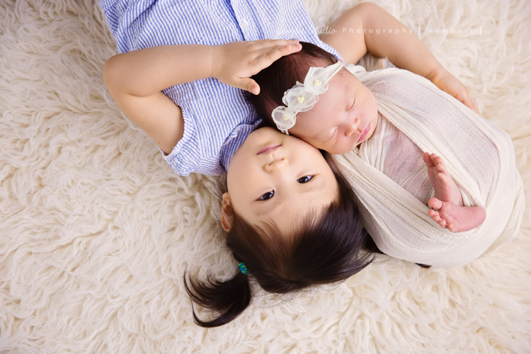 琄媽麻第二個寶貝的新生兒寫真，兩歲的小姊姊展現出滿滿的愛與呵護，小小的手輕輕撫摸著妹妹好有愛，而寶寶那努力撐著小頭的模樣，真是讓人一看就融化，怎麼看都看不膩，這張是寶寶包在白色的布裡、頭上戴著有白色的花的髮帶，小姊姊躺在寶寶旁邊溫柔輕輕地摸著她的頭的兩人合照！