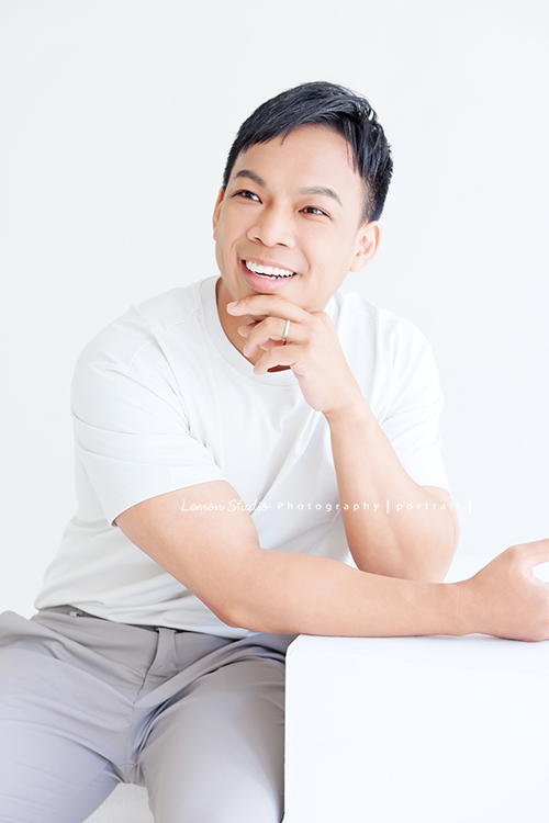 身材壯碩、個性開朗的整復爸爸來拍照，曾是人氣健身教練的他，現在是兩個孩子的爸，把重心放在整復專業上，現為全職整復師，這張是整復爸爸穿白色的上衣，坐著一手放桌面、一手托著下巴，在談話當中捕捉到的沒有看鏡頭微笑的一張很迷人的形象照！