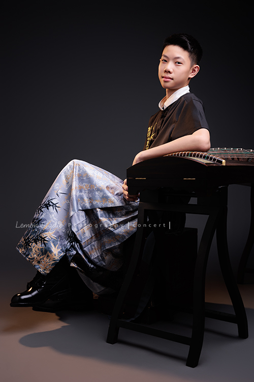 Benson帶著古箏走進鏡頭，穿上馬面裙的那一刻，彷彿穿越時空回到古代，同時又有如舞台上的模特兒般自信，一次拍下古韻與現代交織的獨特風格，這張是Benson穿著馬面裙、側身坐在古箏旁，一手放在古箏上，看著鏡頭微笑著、一張很有意境的音樂會寫真！