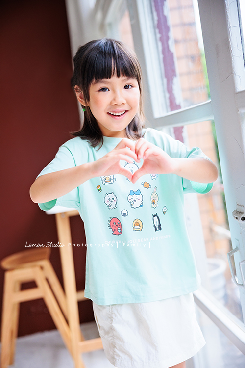 Cheryl媽麻一家第二次來拍照，兄妹倆的成長清晰可見，爸媽的用心陪伴，化作最溫暖的背景，這張是妹妹比愛心並開心地笑著的一張個人寫真！