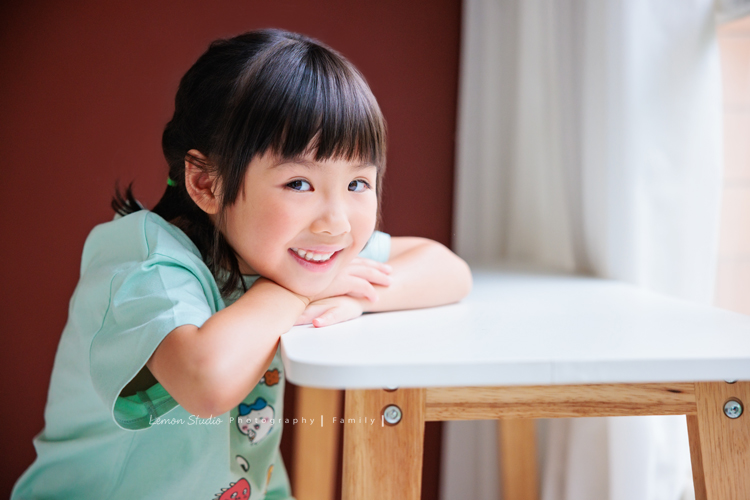 Cheryl媽麻一家第二次來拍照，兄妹倆的成長清晰可見，爸媽的用心陪伴，化作最溫暖的背景，這張是妹妹雙手在桌上、臉靠在手上，笑容很甜美的一張個人寫真！