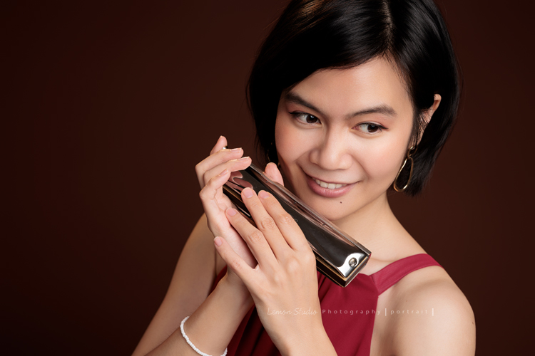 知名口琴演奏家衍華，近日為音樂形象照拍攝，緩緩展開她與音樂的對話，歷經無數舞台洗禮，屢獲殊榮並擔任評審的她，舉手投足間皆是樂音流動的痕跡，彷彿音符化形，翩然於鏡頭之中，這張是衍華身穿紅色的禮服手拿著口琴靠近臉旁，沒有看鏡頭微笑的一張很美很有意境的音樂形象照！