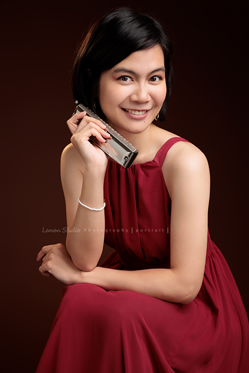 知名口琴演奏家衍華，近日為音樂形象照拍攝，緩緩展開她與音樂的對話，歷經無數舞台洗禮，屢獲殊榮並擔任評審的她，舉手投足間皆是樂音流動的痕跡，彷彿音符化形，翩然於鏡頭之中，這張是衍華身穿紅色的禮服坐在椅子上、一手拿著口琴放在臉旁，看著鏡頭微笑的一張很美的音樂形象照！